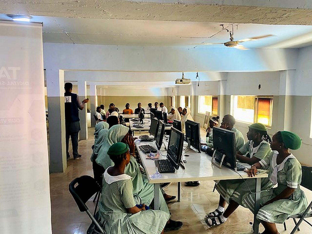 Girls in school uniform working at computer stations during a TADSEF digital literacy session